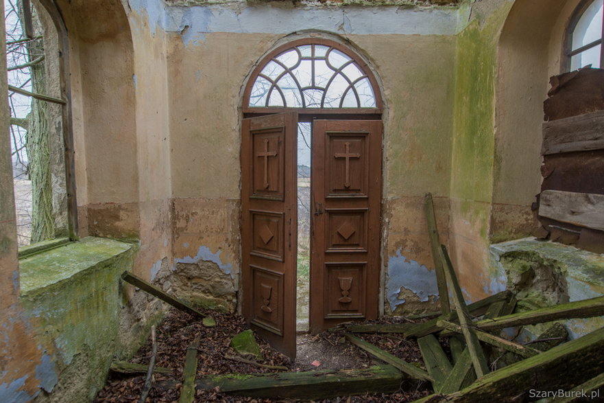 Drzwi kościoła ozdobione płaskimi wizerunkami krzyża i kielicha.