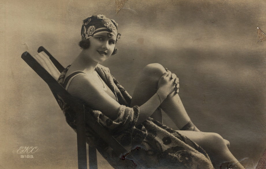 Kobieta siedząca na leżaku. Pocztówka ze zbiorów Biblioteki Narodowej