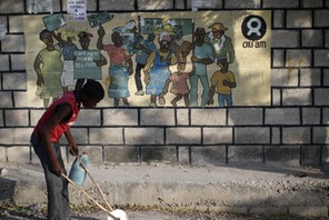 A boy playing with a homemade toy walks past an Oxfam sign in Corail, a camp for displaced people of