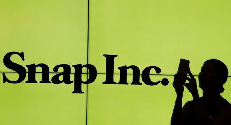 A woman stands in front of the logo of Snap Inc. on the floor of the New York Stock Exchange (NYSE) while waiting for Snap Inc. to post their IPO, in New York City