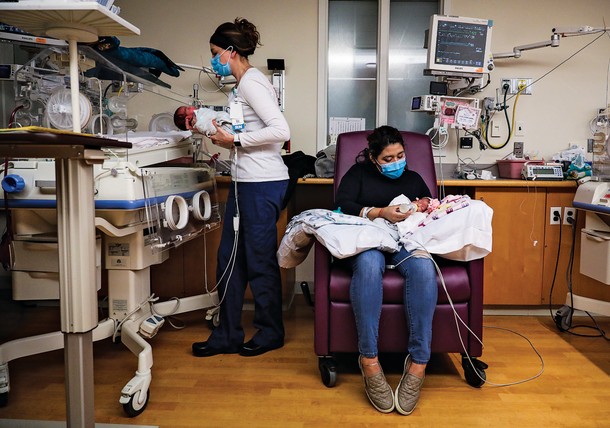 Dayla Sampson, left, places  Sebastian Guevara Hernandez into his bassinet while his mother Lisseth Hernandez feeds his twin Aurora in the NICU at Tufts Medical Center in Boston on May 13, 2020