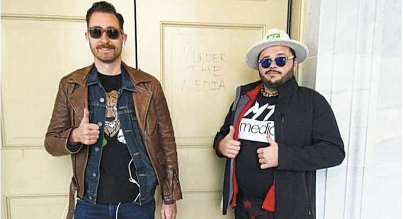 Nicholas Ochs and Nicholas DeCarlo posing outside a Capitol door that has murder the media scrawled in it.