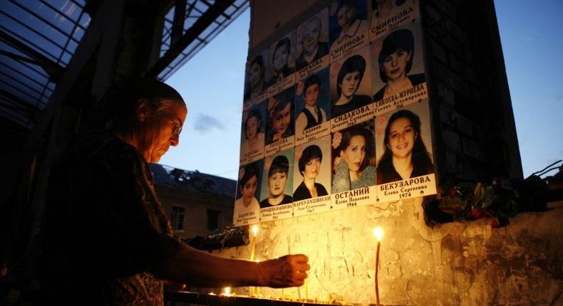 A woman lights candles in front of victims' portraits in the burned-out gymnasium of Beslan's School No. 1.