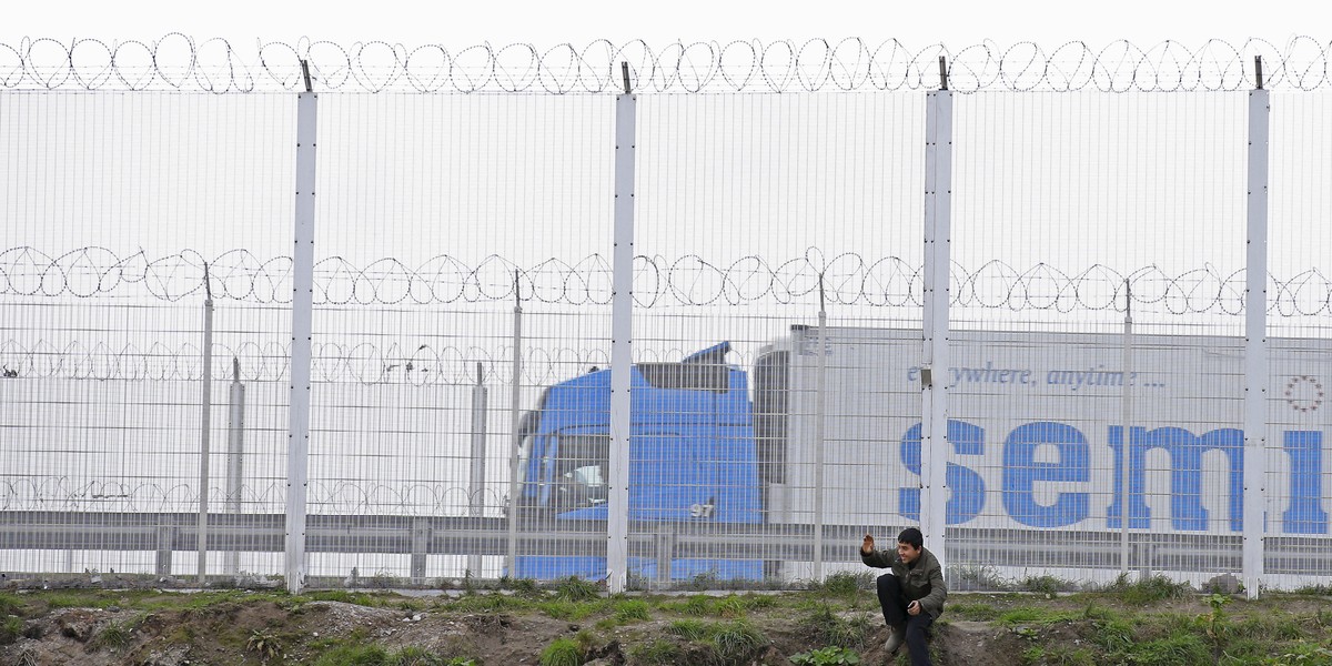 A migrant walks sits in front of a security fence topped with barbed and razor wire on the main access route to the Ferry Harbour Terminal, close the camp known as the "Jungle", a squalid sprawling camp in Calais, northern France, February 6, 2016.