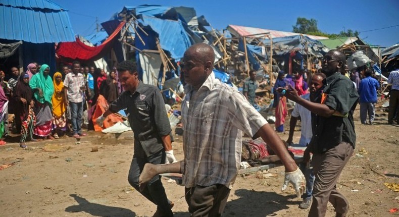 Soldiers assisted by some residents carry the body of a victim from the scene of a suicide car bomb attack at a market in Somalia's capital, Mogadishu on November 26, 2016