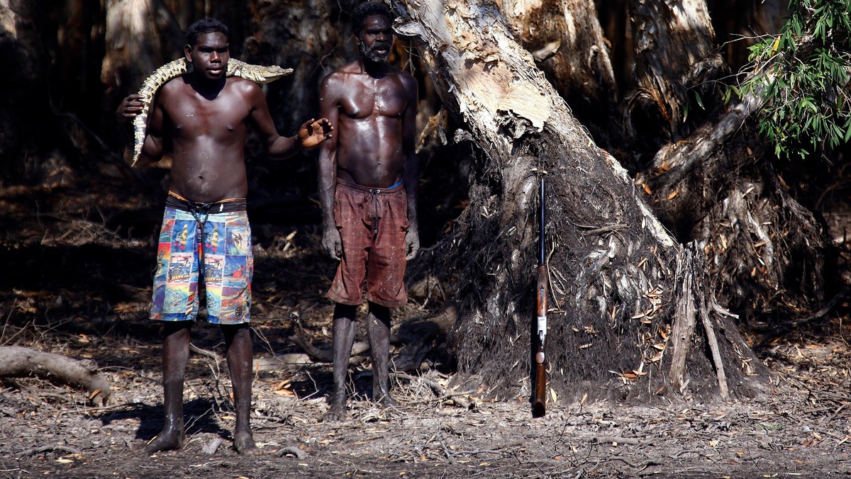 Australian Aboriginal hunter Roy Gaykamangu stands with his son Marcus who carries a baby crocodile on his shoulders on the edge of a billabong near the 'out station' of Yathalamarra in East Arnhem Land