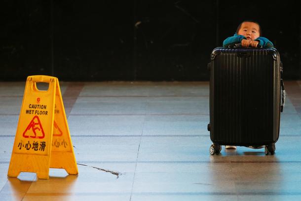 A boy tries to lift a suitcase at the departure hall of the Beijing Railway Station in central Beiji