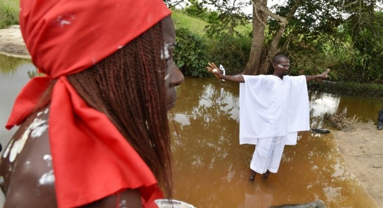 A member of a traditional group stands in the Bodo River with an egg in either hand during the inauguration ceremony of a memorial stone on a site of the former slave route in the Ivorian hamlet of Kanga Gnianze, northwest of Abidjan