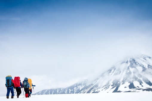 Group with gear and backpacks crossing icy field to mountain