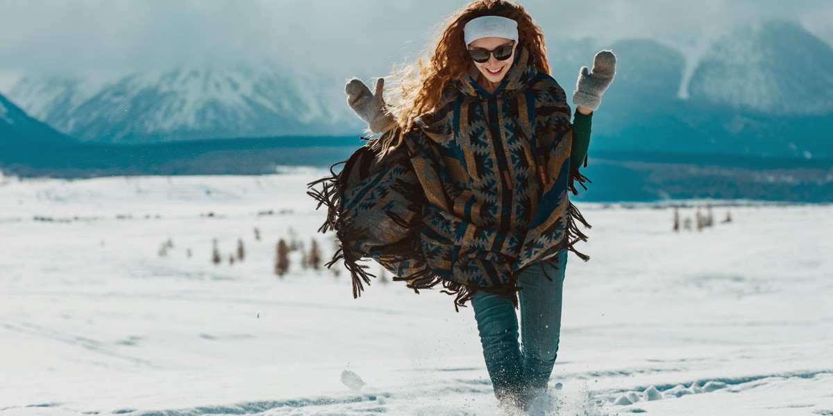 Happy young girl dressed in poncho runs in snow