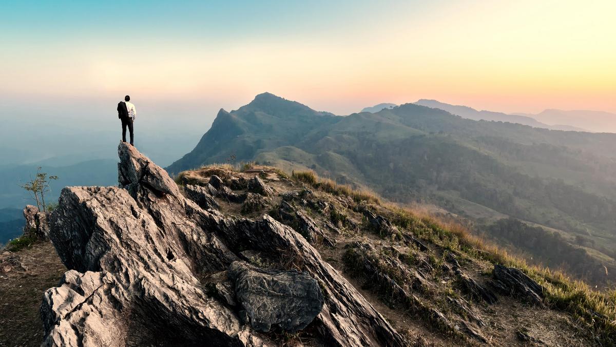 businessman hike on the peak of rocks mountain at sunset