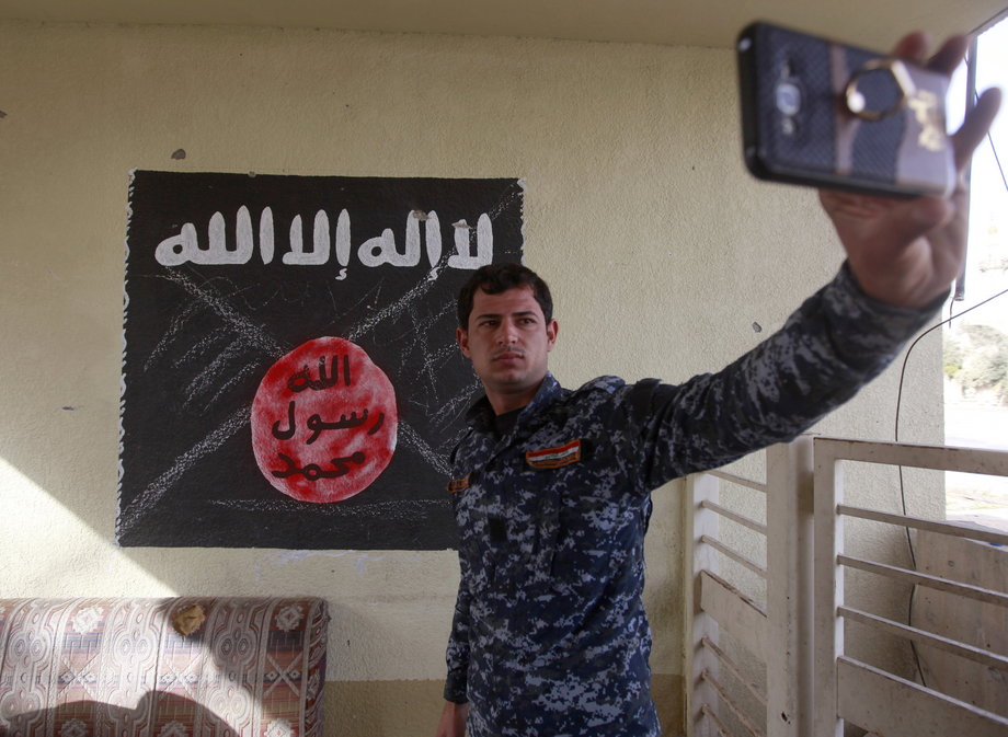 A member of the federal-police forces takes a selfie in front of a defaced black flag commonly used by ISIS militants, during a battle with ISIS militants in the Wahda district of eastern Mosul, Iraq, January 10, 2017.