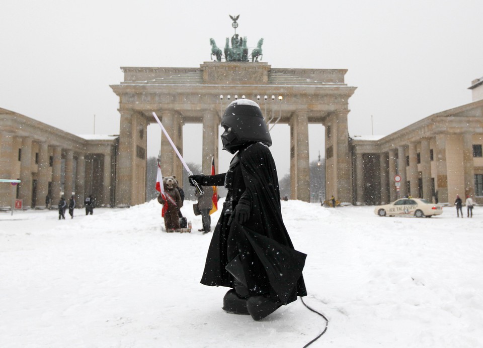 A street performer dressed as the character 'Darth Vader' from the film 'Star Wars' stands in front of the Brandenburg Gate during snowfall in Berlin