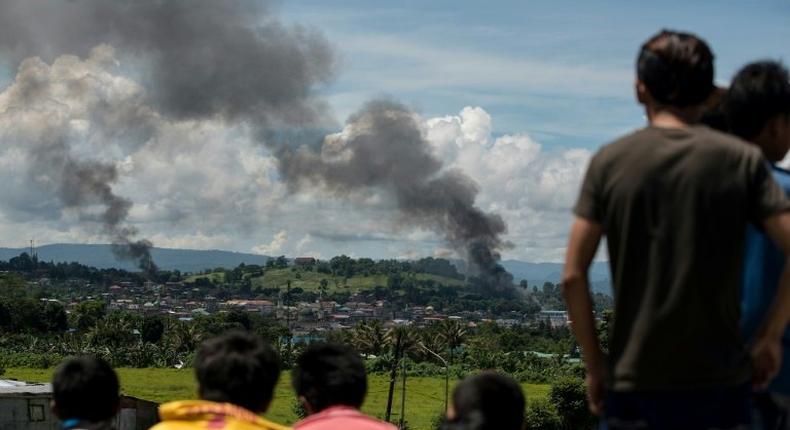 People watch as smoke rises from houses after Philippine air force planes bombed Islamist militant positions in the city of Marawi on the southern island of Mindanao