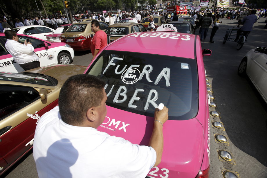 A local taxi driver paints "Uber out" on the back windshield of his car during a protest in Mexico City, May 25, 2015.