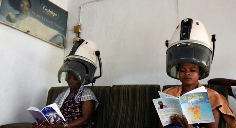 Women sitting under hair steamers read books from a mini-library at a hairdresser's in Abidjan.