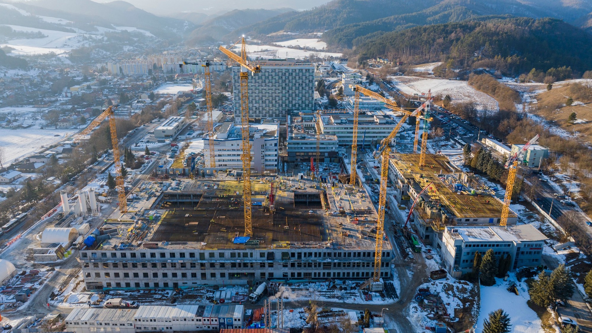 Stavba novej nemocnice v Banskej Bystrici. V pozadí vidno zrekonštruovanú Detskú fakultnú nemocnicu (vľavo), vedľa nej polikliniku a za nimi ikonickú lôžkovú časť Rooseveltovej nemocnice. Január 2026.