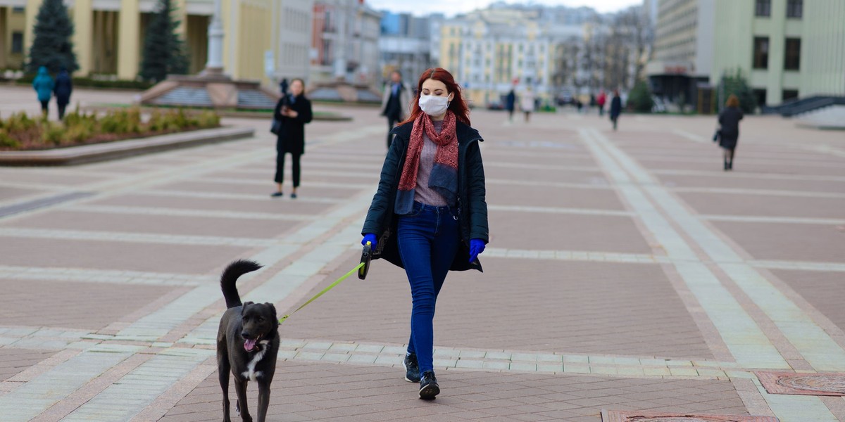 Young female using a face mask as a coronavirus spreading prevention walking with her dog. Global CO