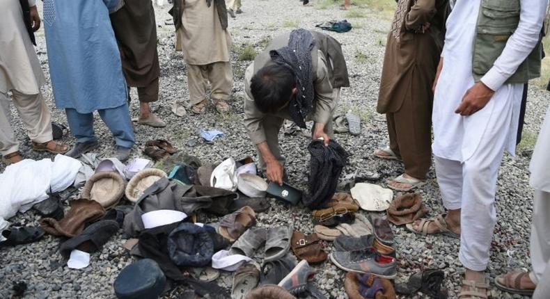 Afghan men examine the belongings of blast victims at the site of a series of explosions that targeted a funeral of a politician's son, who was killed during an anti-government protest a day earlier in Kabul