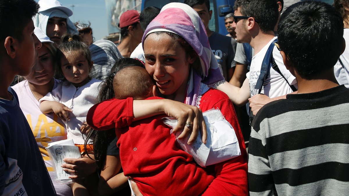 A woman holding a baby and her registration papers cries, as refugees and migrants wait to board a bus that will transfer them from a makeshift camp at the port of Piraeus to a newly built relocation centre in the port town of Skaramagkas, in western Athe