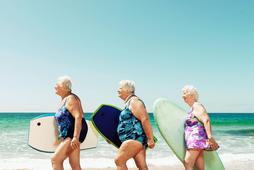 Three mature women on beach with surfboards