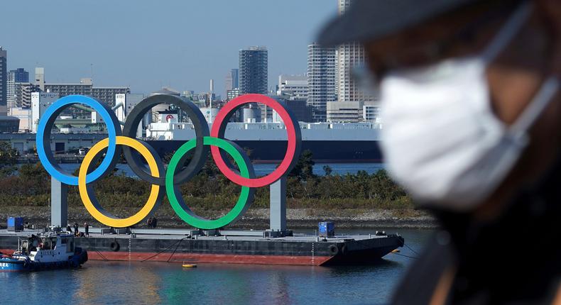 A man wearing a protective face mask in front of the Olympic rings in Tokyo.
