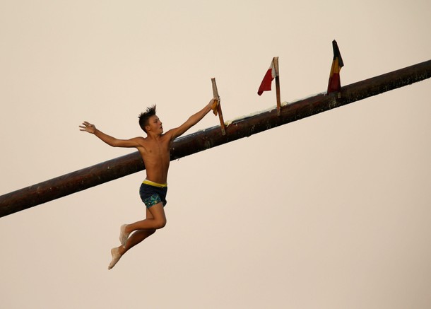 A child competitor grabs a flag as he falls off the gostra, a wooden pole covered in lard, during 