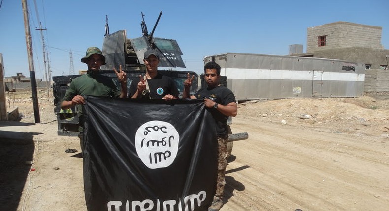 Iraqi security forces stand with an Islamic State flag which they pulled down in the town of Hit in Anbar province, April 2, 2016. 