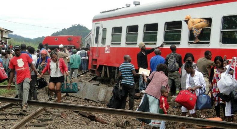 A passenger escapes a train car using a window as others leave from the site of a train derailment in Eseka on October 21, 2016