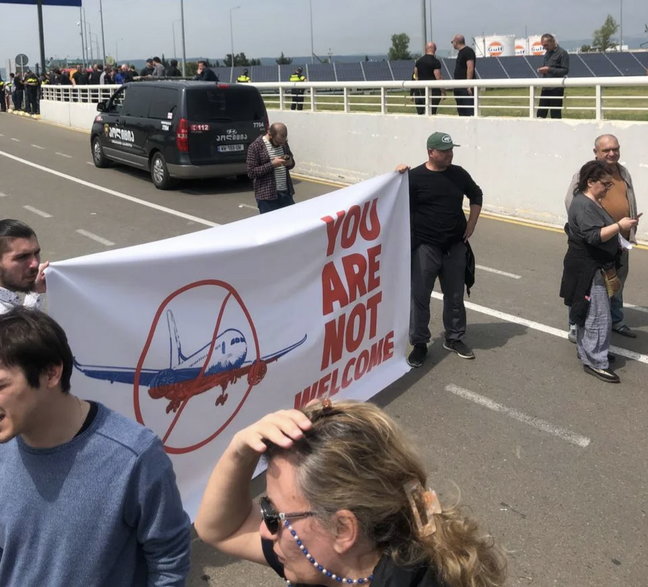 Transparent "Nie jesteście tu mile widziani" przed lotniskiem w Tbilisi, gdzie wylądował właśnie pierwszy od czterech lat samolot z Rosji. 19 maja 2023 r.