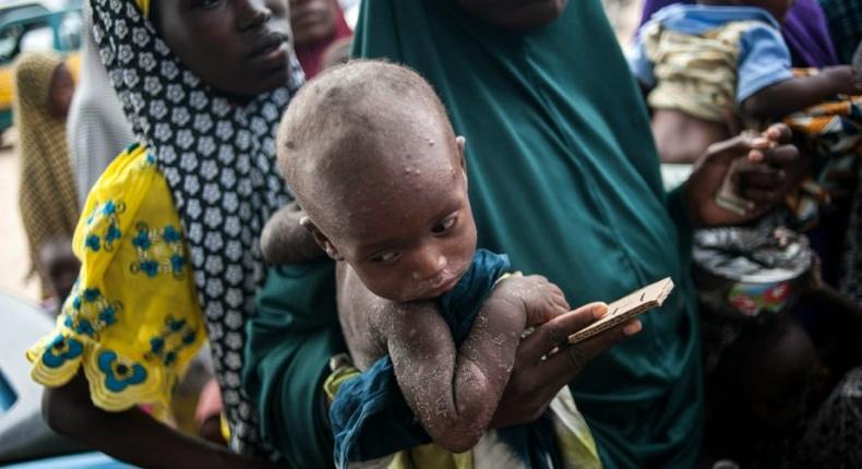 A woman holds her child while waiting in a queue at one of the UNICEF nutrition clinics in Muna informal settlement, in northeastern Nigeria in June 2016