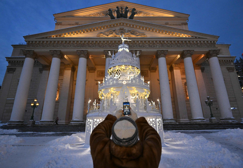 Kobieta robi zdjęcie telefonem komórkowym dekoracjom świąteczno-noworocznym przed Teatrem Bolszoj w centrum Moskwy 20 grudnia 2022 r.