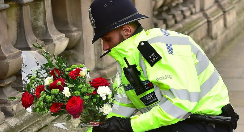 A police officer places flowers and a photo of Pc Keith Palmer on Whitehall near the Houses of Parliament in London, after seven people were arrested in raids in London, Birmingham and elsewhere linked to the Westminster terror attack.
