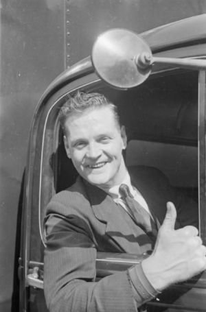 Uśmiechnięty brytyjski kierowca ciężarówki pokazujący uniesiony kciuk, 1940 r. (domena publiczna).