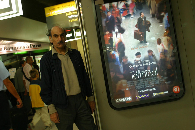 Mehram Karimi Nasseri obok plakatu zapowiadającego premierę filmu "Terminal" na podstawie jego życiowej historii