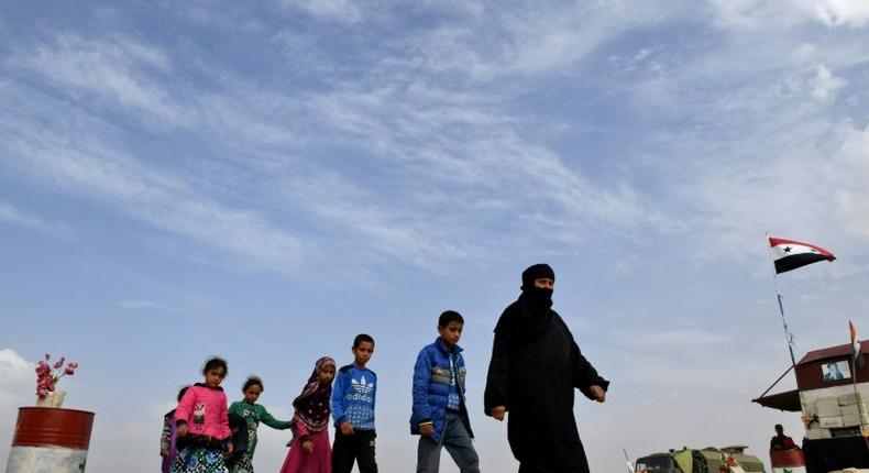 Syrian families walk as members of Russian and Syrian forces stand guard at the Abu Duhur crossing on the eastern edge of Syria's Idlib province on October 23, 2018.Civilians are coming from rebel-held areas in Idlib province and entering regime-held territories through the Abu Duhur crossing, some of them returning to their villages that were recaptured by the regime forces earlier this year.