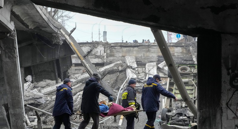 Ukrainian rescue workers carry an elderly woman under a destroyed bridge in Irpin, close to Kyiv, Ukraine, Friday, April 1, 2022.