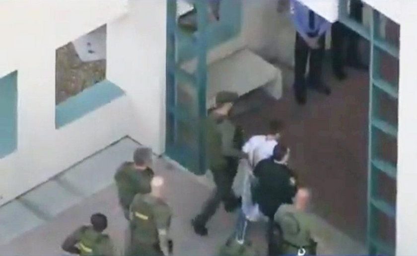 Police escort a suspect into the Broward Jail after checking him at the hospital following a shootin