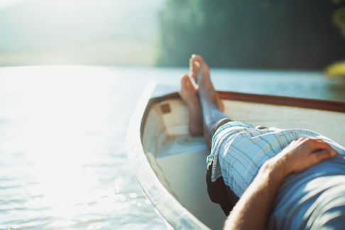 Man laying in rowboat on tranquil lake