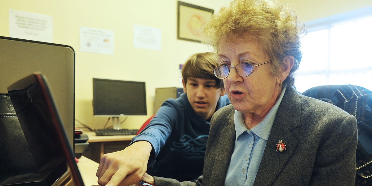 A teenager helps an elderly woman use a computer