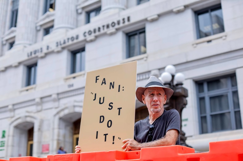 Samotny protestujący trzyma znak przed budynkiem sądu hrabstwa Fulton, Atlanta, Georgia, USA, 7 sierpnia 2023 r.