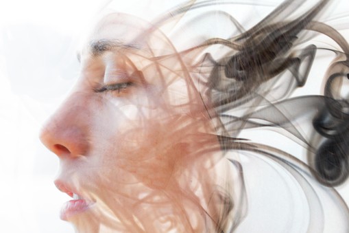 Double exposure portrait of a young fair-skinned woman and a smoky texture dissolving into her facial features