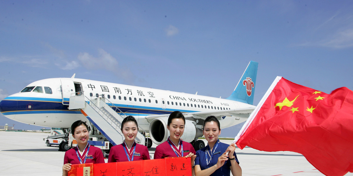 Crew members holding a Chinese national flag pose in front of a plane at a new airport China built on Mischief Reef in the South China Sea.