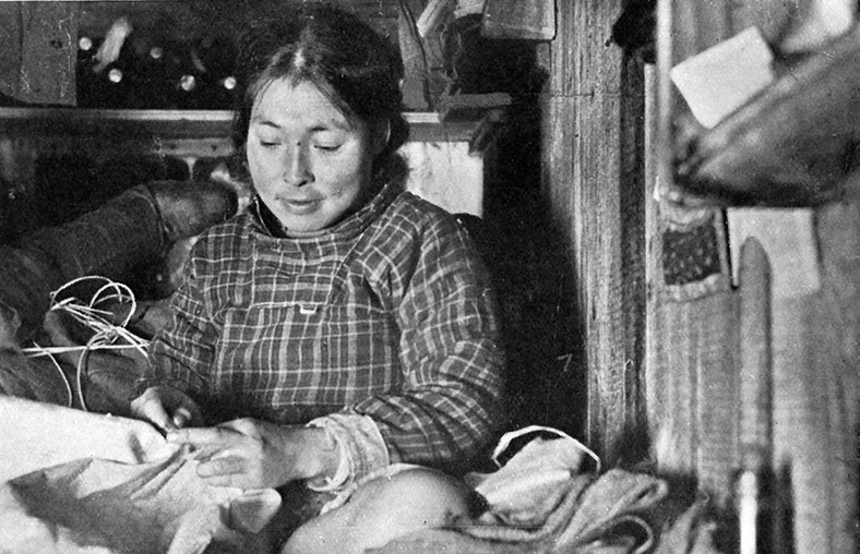 Arnanguaq, żona Arqioqa, naprawiająca odzież. Siedzi w charakterystycznej dla eskimoskich kobiet – i dla krawców w ogólności – pozycji przyjmowanej podczas szycia