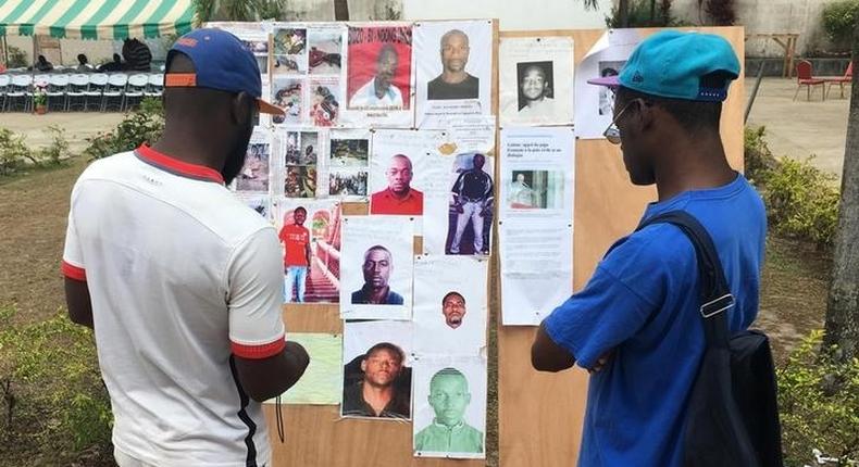 Men examine a poster board showing people who died or are still missing following clashes after elections in Libreville, Gabon, September 19, 2016. 