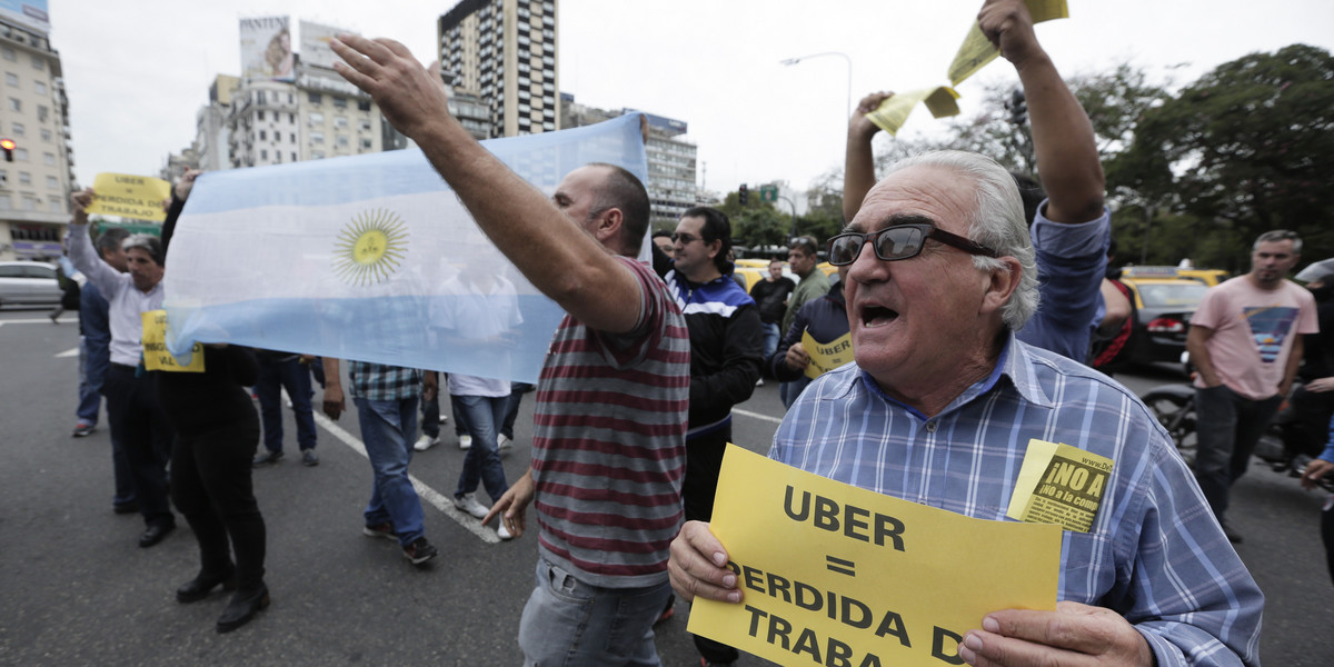 A taxi driver holds a sign that says in Spanish "Uber equals job loss" as he and other cabbies block a main avenue in Buenos Aires, Argentina, Tuesday, April 12, 2016.