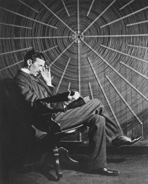 Tesla siedzący przed spiralną cewką używaną w eksperymentach z zasilaniem bezprzewodowym