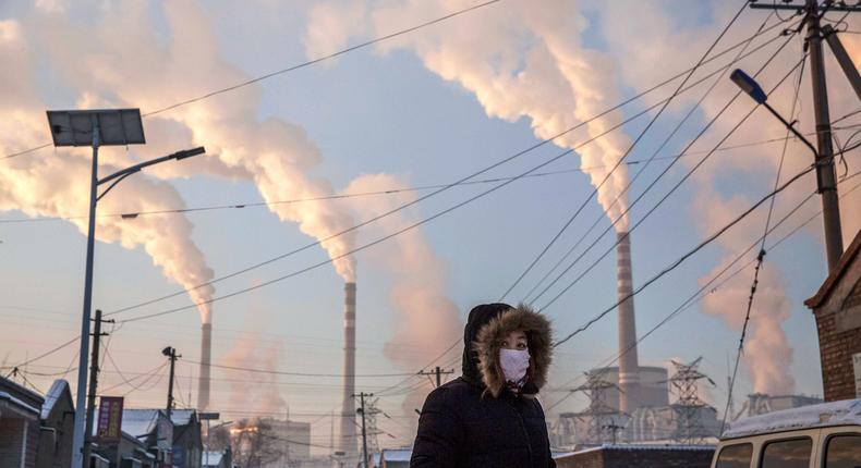 Smoke billows from coal-fired power plant stacks as a Chinese woman wears a protective mask.