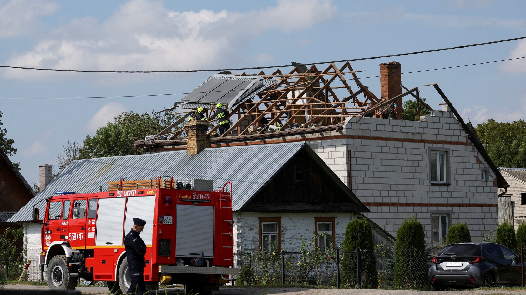 Policajt sleduje hasičov pracujúcich na zničenej streche domu po tom, čo ruské drony narušili poľský vzdušný priestor.