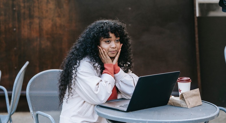 Dreamy black woman sitting in street cafe with laptop [Photo: Uriel Mont]